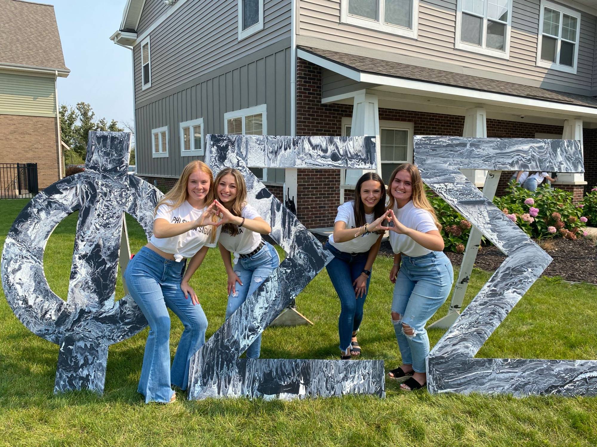 Phi Sigma Sigma sisters posing in front of their house and letters